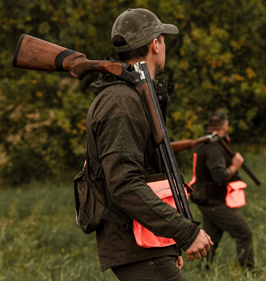 Two hunters in a field with shotguns and backpacks